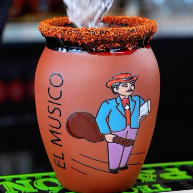 A Padrino’s Mexican drink in a clay jar with a chili-lime rim and a cartoon mariachi.