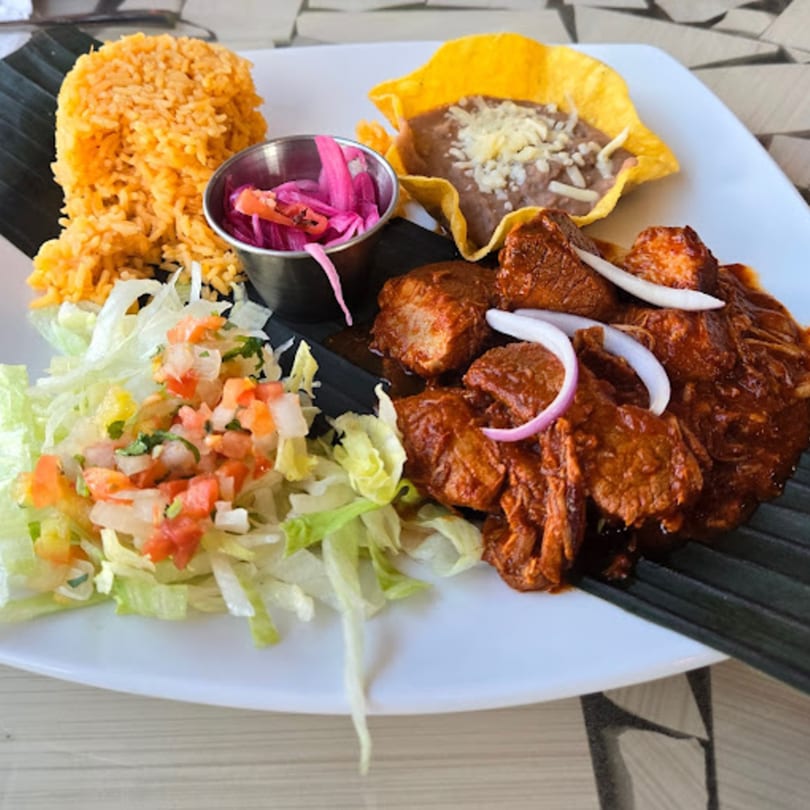 Padrino's Mexican dish with red rice, refried beans in a tortilla bowl, saucy pork, and salad.