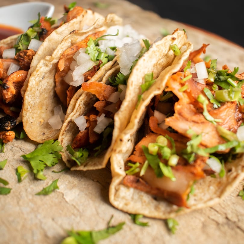 Three Padrino's Mexican tacos with meat, cilantro, and diced onions on a wooden surface.