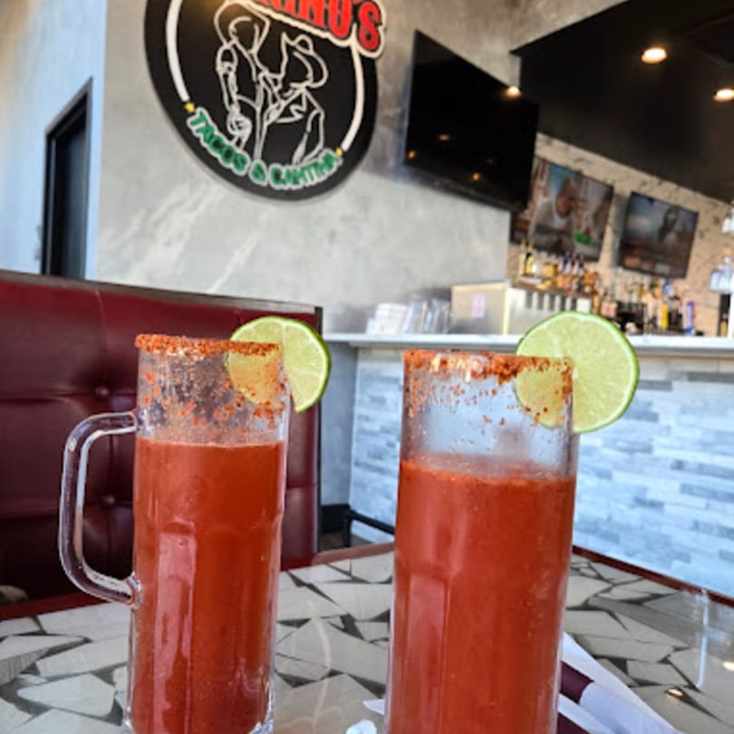 Two red micheladas with lime wedges and chili salt rims on a table at Padrino's.