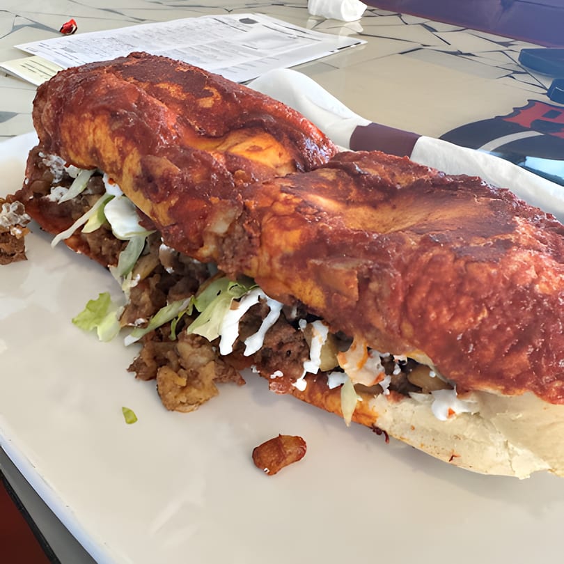 A large, saucy Mexican torta with meat, lettuce, and crema on a white plate.