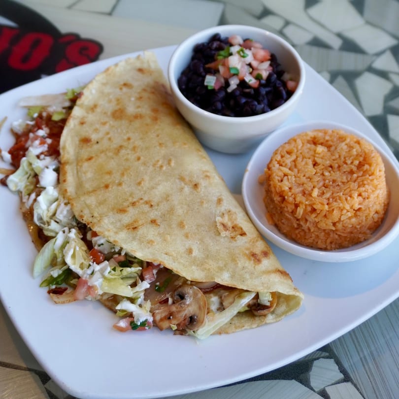 A Padrino's Mexican quesadilla with mushrooms, lettuce, and sour cream, served with black beans and rice.