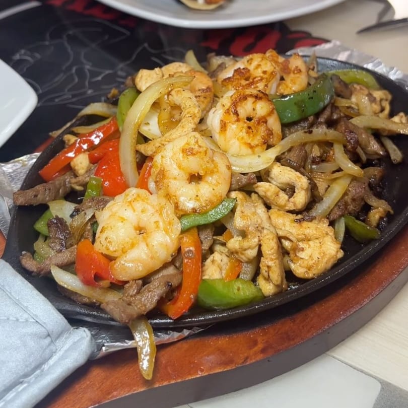 Sizzling Padrino's fajitas with shrimp, chicken, beef, onions, and bell peppers on a hot plate.